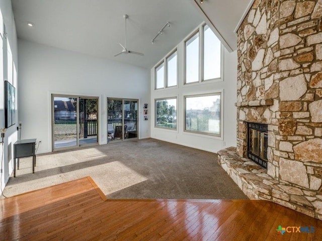 unfurnished living room with baseboards, a ceiling fan, wood-type flooring, a fireplace, and high vaulted ceiling