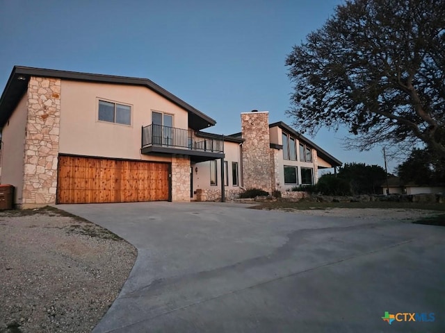 view of front of property with stone siding, a balcony, concrete driveway, and stucco siding