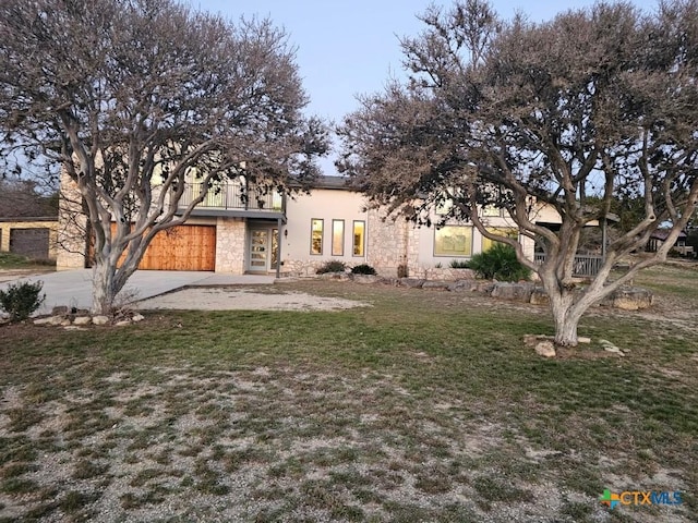 view of front of home with an attached garage, concrete driveway, stone siding, stucco siding, and a front yard