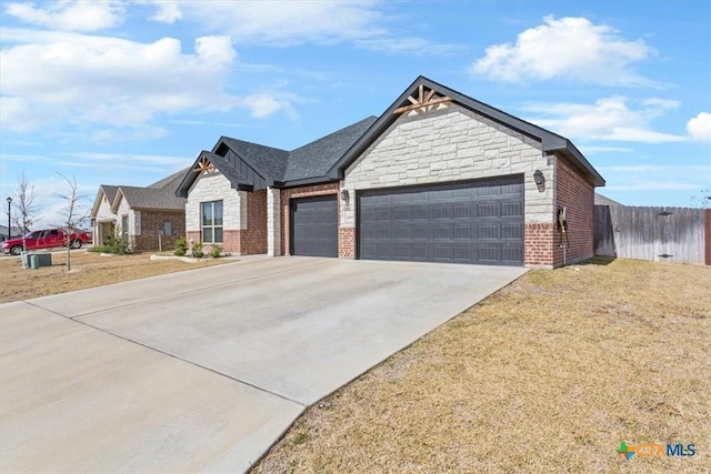 view of front of home featuring an attached garage, brick siding, fence, stone siding, and driveway