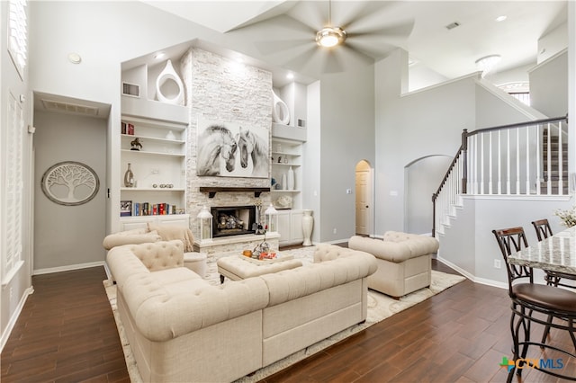 living room with ceiling fan, high vaulted ceiling, a stone fireplace, dark wood-type flooring, and built in features