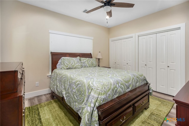 bedroom featuring wood-type flooring, two closets, and ceiling fan