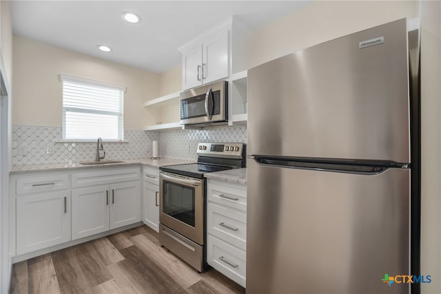 kitchen with stainless steel appliances, light stone countertops, sink, light hardwood / wood-style floors, and white cabinets