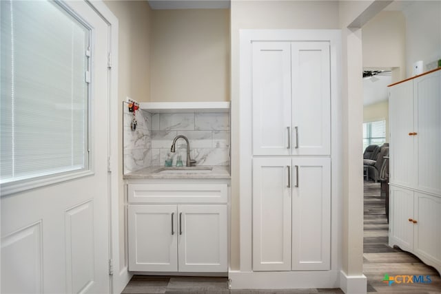 bar with white cabinets, hardwood / wood-style flooring, light stone counters, and sink