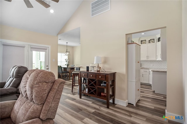 living room featuring wood-type flooring, ceiling fan with notable chandelier, and high vaulted ceiling