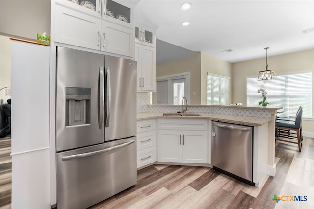 kitchen with light hardwood / wood-style floors, stainless steel appliances, decorative backsplash, sink, and white cabinetry