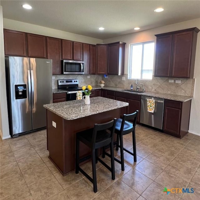 kitchen with a kitchen island, light stone counters, decorative backsplash, stainless steel appliances, and a sink