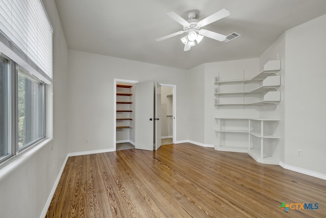 unfurnished bedroom featuring a closet, a walk in closet, ceiling fan, and light hardwood / wood-style flooring