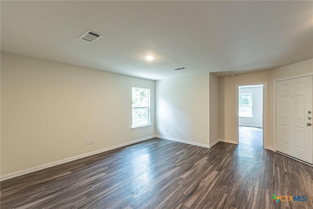 unfurnished room with a textured ceiling, dark wood-type flooring, and a healthy amount of sunlight