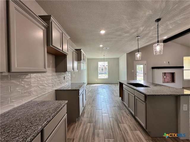2591 Cedar Glen Dr, Belton, TX 76513 - kitchen featuring dark stone counters, a kitchen island with sink, black electric cooktop, decorative backsplash, and vaulted ceiling