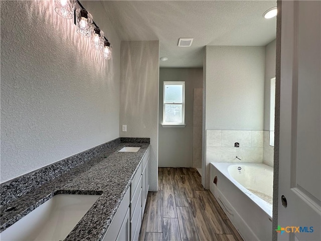 2591 Cedar Glen Dr, Belton, TX 76513 - bathroom featuring a bath, double vanity, a textured wall, a textured ceiling, and wood finished floors