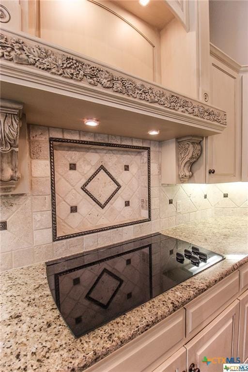 kitchen featuring decorative backsplash, cream cabinets, black electric cooktop, and light stone counters