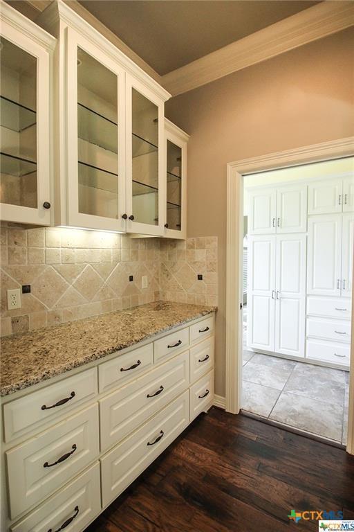 kitchen featuring dark wood-type flooring, white cabinets, decorative backsplash, light stone countertops, and ornamental molding