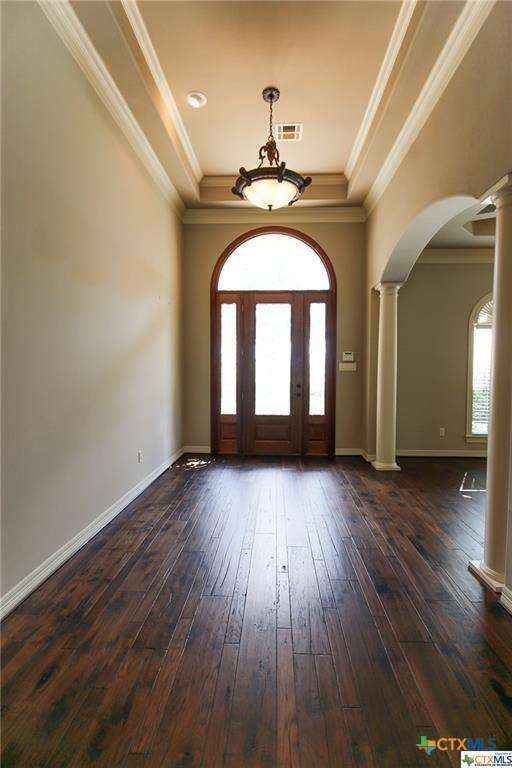 entrance foyer with dark hardwood / wood-style floors, a wealth of natural light, ornamental molding, and decorative columns