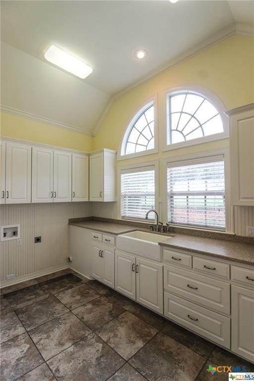 kitchen featuring wood walls, white cabinetry, lofted ceiling, and sink