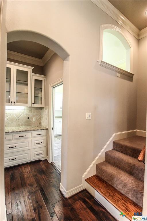 kitchen featuring light stone counters, dark hardwood / wood-style flooring, crown molding, decorative backsplash, and white cabinets