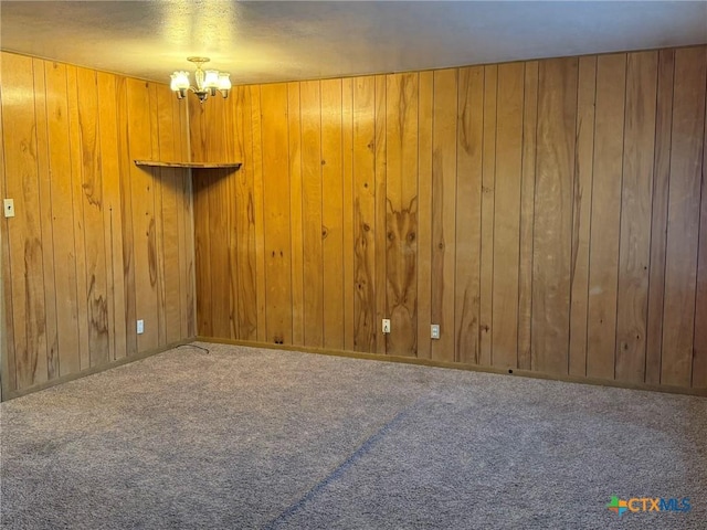 spare room featuring a notable chandelier, wood walls, and carpet flooring