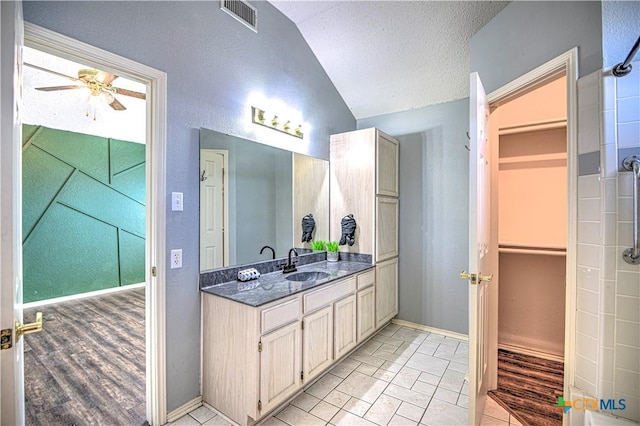 full bath with visible vents, a textured ceiling, vanity, lofted ceiling, and a spacious closet