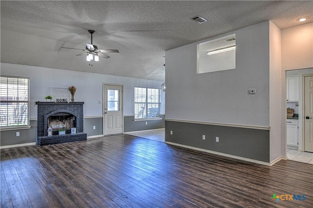 unfurnished living room with visible vents, a brick fireplace, lofted ceiling, wood finished floors, and a ceiling fan