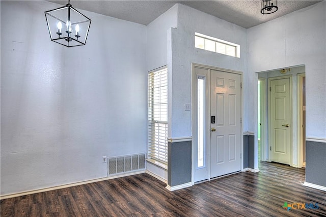 entrance foyer with visible vents, a textured ceiling, dark wood finished floors, an inviting chandelier, and baseboards