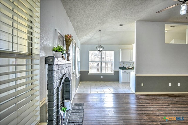 unfurnished living room featuring light wood finished floors, visible vents, lofted ceiling, a fireplace, and a textured ceiling