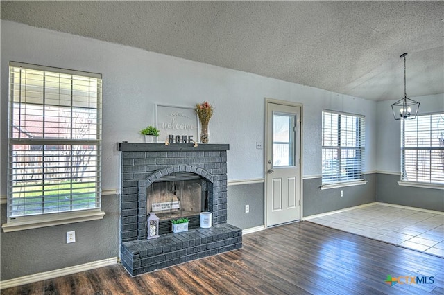 unfurnished living room featuring a chandelier, wood finished floors, a fireplace, a textured wall, and a textured ceiling