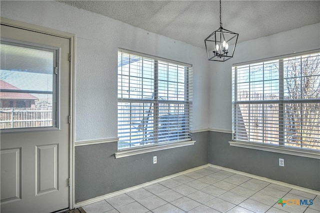 unfurnished dining area featuring tile patterned flooring, baseboards, an inviting chandelier, a textured wall, and a textured ceiling