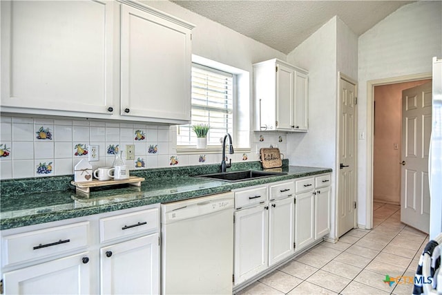 kitchen featuring dark countertops, dishwasher, light tile patterned flooring, white cabinets, and a sink