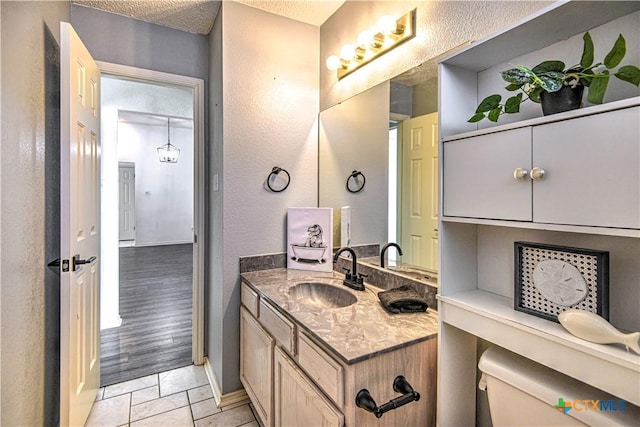 bathroom with baseboards, a textured ceiling, vanity, and a textured wall