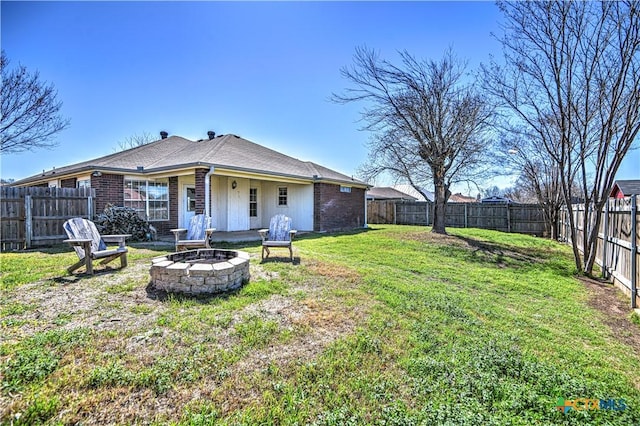 back of house featuring brick siding, a lawn, a fire pit, and a fenced backyard