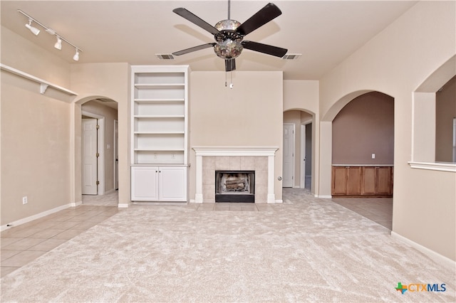 unfurnished living room featuring light carpet, built in shelves, a fireplace, and ceiling fan