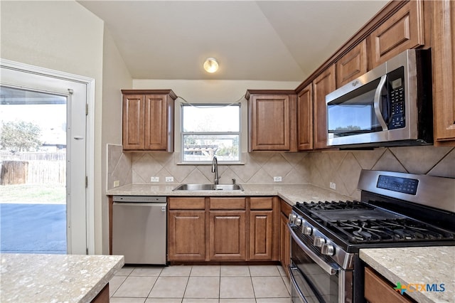 kitchen with sink, vaulted ceiling, tasteful backsplash, light tile patterned flooring, and stainless steel appliances