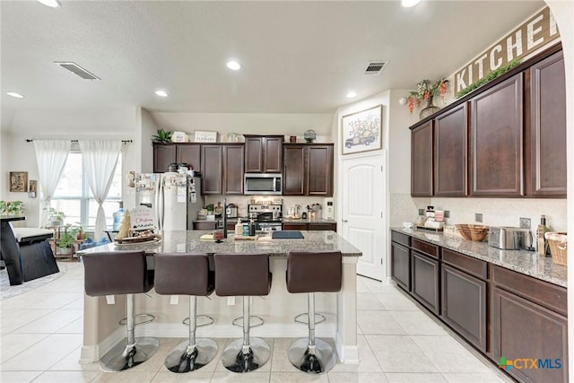 kitchen with a breakfast bar, light stone countertops, a center island with sink, and stainless steel appliances