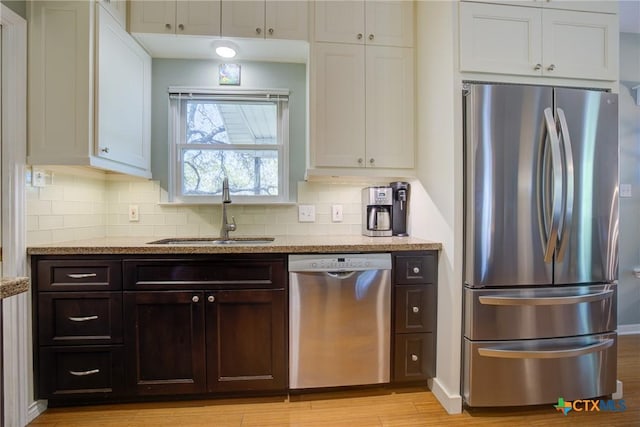 kitchen with tasteful backsplash, white cabinets, a sink, appliances with stainless steel finishes, and light stone countertops