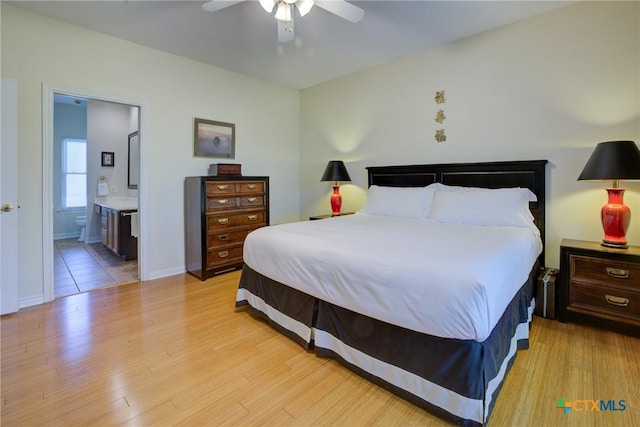 bedroom with light wood-style flooring, ceiling fan, ensuite bath, and baseboards
