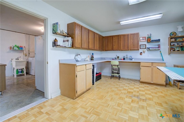 kitchen featuring open shelves, a sink, light countertops, washer / dryer, and brown cabinets