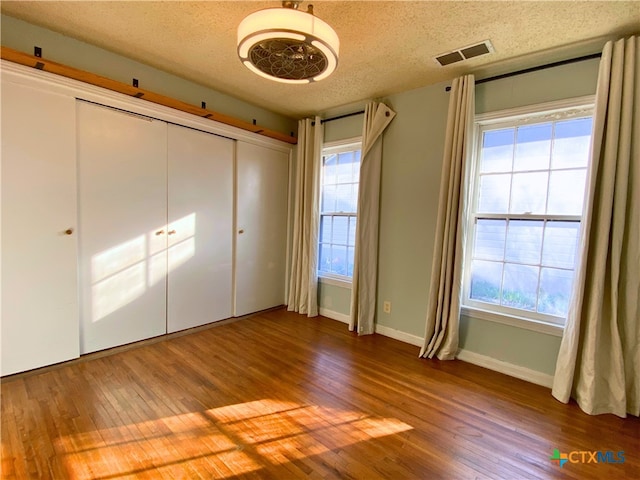 unfurnished bedroom with a closet, multiple windows, a textured ceiling, and hardwood / wood-style floors