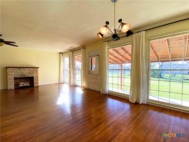 unfurnished living room with ceiling fan with notable chandelier, dark hardwood / wood-style flooring, a fireplace, and a healthy amount of sunlight