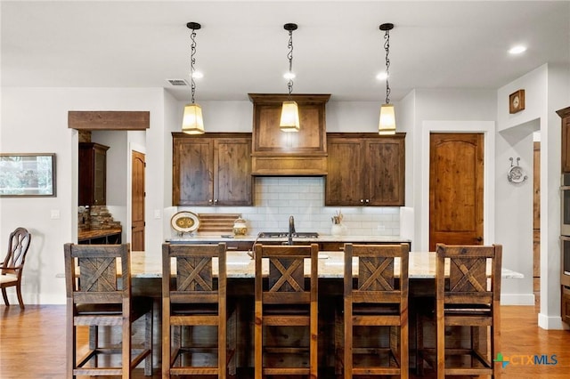 1204 Salt Lick Dr, New Braunfels, TX 78132 - kitchen featuring decorative backsplash, dark wood-style flooring, a breakfast bar area, an island with sink, and pendant lighting