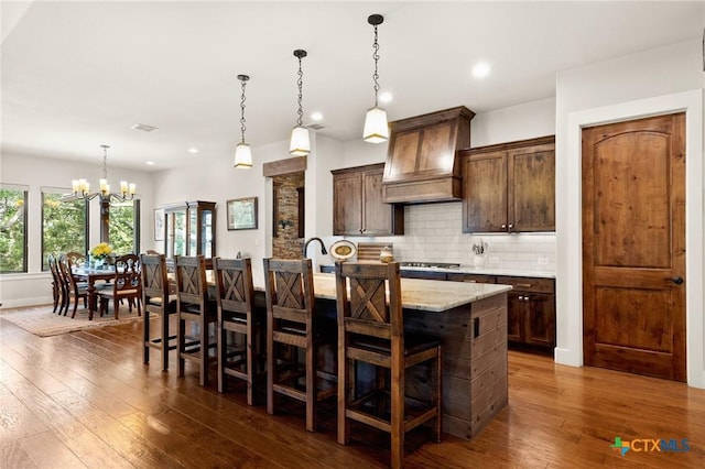 1204 Salt Lick Dr, New Braunfels, TX 78132 - kitchen with custom exhaust hood, a chandelier, backsplash, a kitchen island with sink, and dark wood-style flooring
