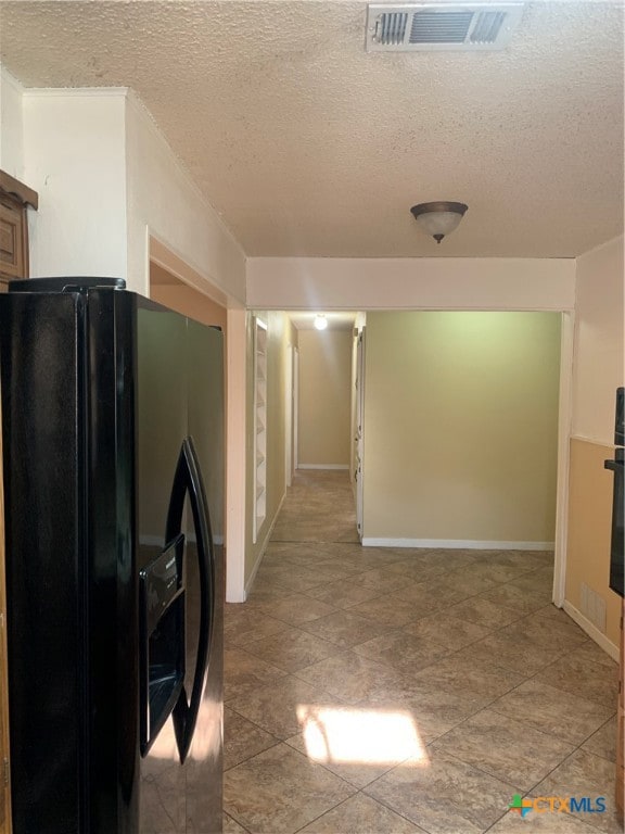 interior space featuring black fridge with ice dispenser and a textured ceiling