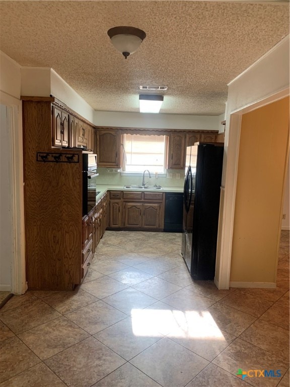 kitchen featuring black appliances, sink, light tile patterned floors, and a textured ceiling