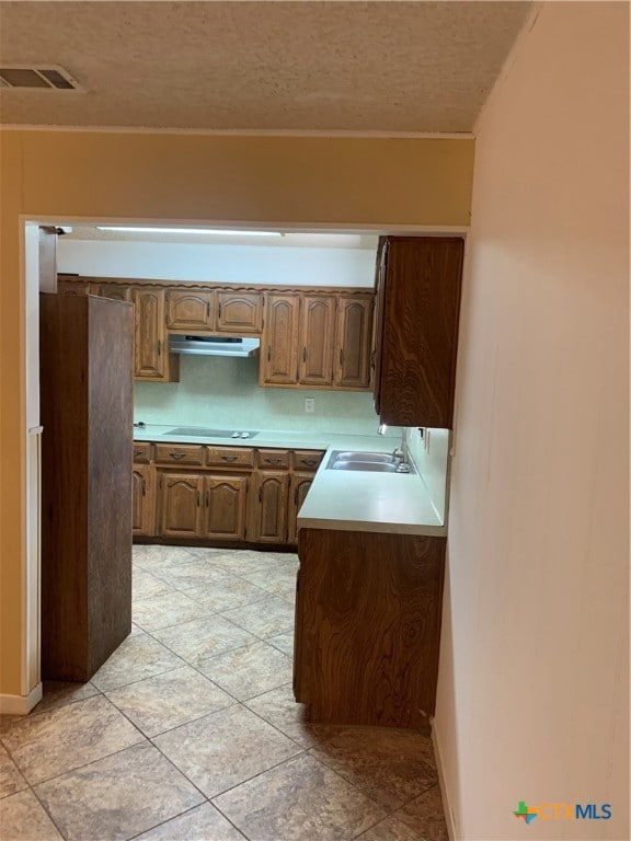 kitchen with a textured ceiling, sink, cooktop, and light tile patterned floors