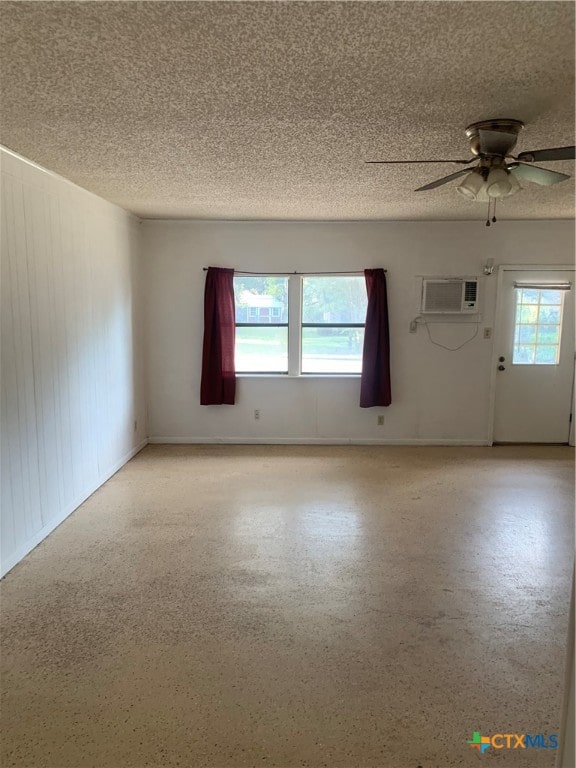 spare room with an AC wall unit, a textured ceiling, ceiling fan, and plenty of natural light