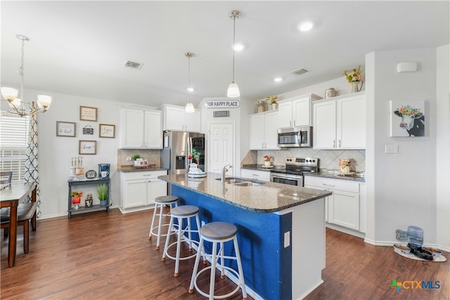 kitchen with stainless steel appliances, decorative light fixtures, dark hardwood / wood-style floors, white cabinetry, and an island with sink