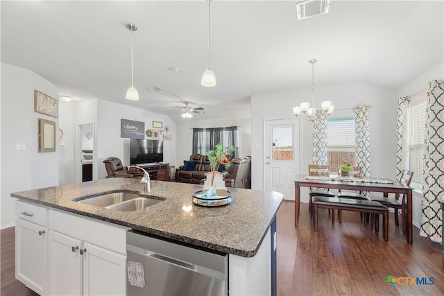 kitchen with stainless steel dishwasher, ceiling fan with notable chandelier, dark wood-type flooring, white cabinets, and an island with sink