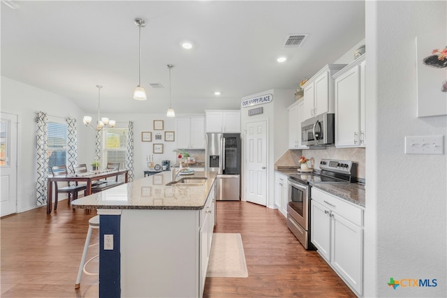 kitchen with pendant lighting, a center island with sink, stainless steel appliances, and wood-type flooring