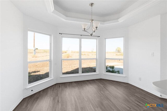 unfurnished dining area with dark wood-type flooring, a wealth of natural light, an inviting chandelier, and a raised ceiling