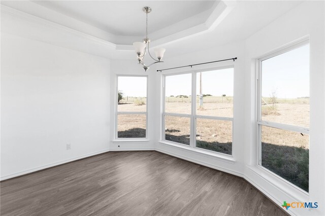 unfurnished dining area featuring dark hardwood / wood-style flooring, an inviting chandelier, and a raised ceiling