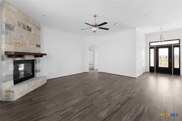 unfurnished living room with a stone fireplace, dark hardwood / wood-style floors, crown molding, and ceiling fan